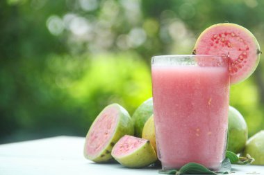 Guava suyu, cam bardakta taze guava suyu ve doğal arka planda guava dilimleri.