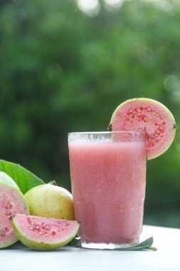 Guava suyu, cam bardakta taze guava suyu ve doğal arka planda guava dilimleri.