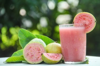 Guava suyu, cam bardakta taze guava suyu ve doğal arka planda guava dilimleri.
