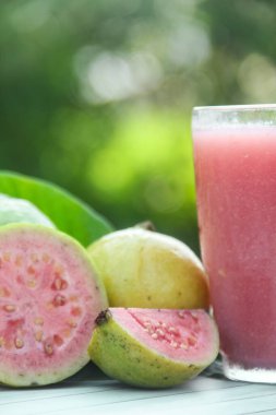 Guava suyu, cam bardakta taze guava suyu ve doğal arka planda guava dilimleri.