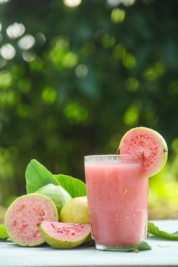 Guava suyu, cam bardakta taze guava suyu ve doğal arka planda guava dilimleri.