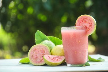 Guava suyu, cam bardakta taze guava suyu ve doğal arka planda guava dilimleri.