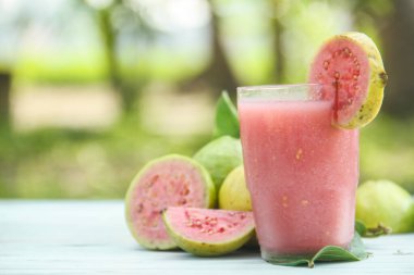 Guava suyu, cam bardakta taze guava suyu ve doğal arka planda guava dilimleri.