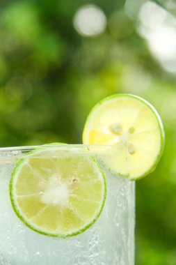 Taze limon dilimli bir bardak soğuk su, ahşap masaya konmuş limon dilimli sağlıklı bir içecek ve doğal arka plan.