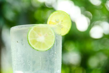 Taze limon dilimli bir bardak soğuk su, ahşap masaya konmuş limon dilimli sağlıklı bir içecek ve doğal arka plan.