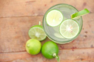 Taze limon dilimli bir bardak soğuk su, ahşap masaya konmuş limon dilimli sağlıklı bir içecek.