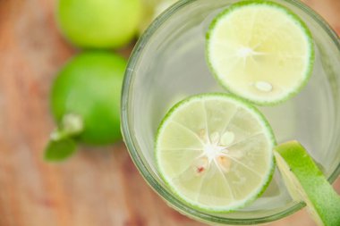 Taze limon dilimli bir bardak soğuk su, ahşap masaya konmuş limon dilimli sağlıklı bir içecek.