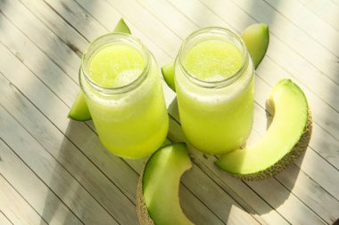 Yanında taze kavun dilimleriyle dekore edilmiş bardakta taze kavun suyu ve bardakta iki bardak taze kavun.