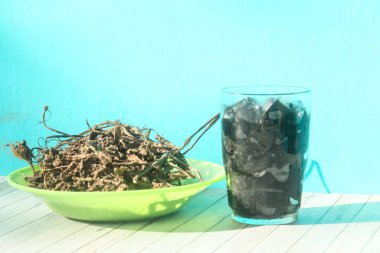 Siyah çimen jölesi parçaları bir bardakta ve kurutulmuş çimen jölesi yapraklarıyla süslenmiş veya siyah çimen jölesi yapmak için hammadde olarak Mesona chinensis