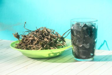 Siyah çimen jölesi parçaları bir bardakta ve kurutulmuş çimen jölesi yapraklarıyla süslenmiş veya siyah çimen jölesi yapmak için hammadde olarak Mesona chinensis