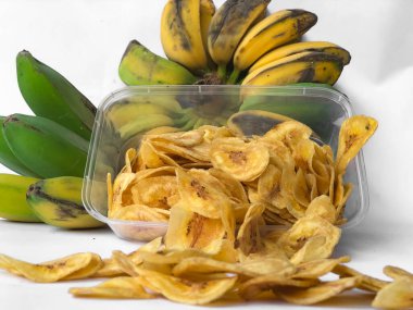 Kepok muz veya musa paradisiaca meyvesi ile süslenmiş ve beyaz bir arkaplanda izole edilmiş muz cipsi serpintisi.