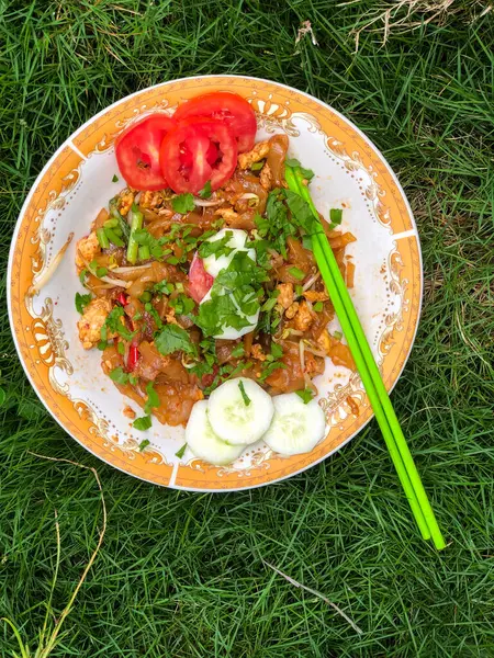 Dilimlenmiş salatalık, domates ve kereviz yaprakları gibi çeşitli garnitürlerle servis edilen bir tabak Tiaw Noodles.