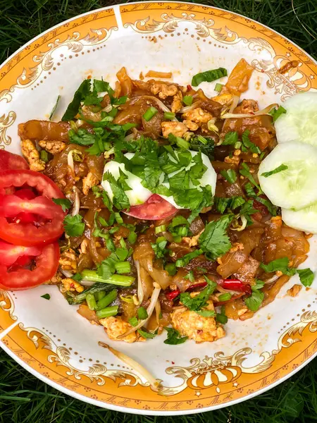 Dilimlenmiş salatalık, domates ve kereviz yaprakları gibi çeşitli garnitürlerle servis edilen bir tabak Tiaw Noodles.