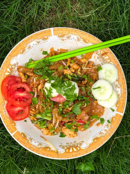 Dilimlenmiş salatalık, domates ve kereviz yaprakları gibi çeşitli garnitürlerle servis edilen bir tabak Tiaw Noodles.