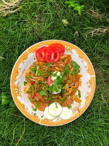 Dilimlenmiş salatalık, domates ve kereviz yaprakları gibi çeşitli garnitürlerle servis edilen bir tabak Tiaw Noodles.