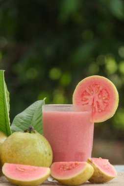 Guava suyu ya da bir bardakta Psidium Guajava ve yeşil yaprakların doğal bir arka planına sahip bir masada tüm ve dilimlenmiş guava ile süslenmiş.