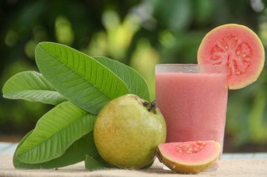 Guava suyu ya da bir bardakta Psidium Guajava ve yeşil yaprakların doğal bir arka planına sahip bir masada tüm ve dilimlenmiş guava ile süslenmiş.