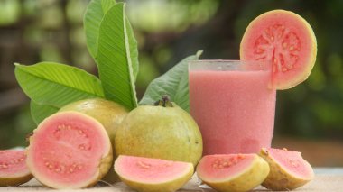 Guava suyu ya da bir bardakta Psidium Guajava ve yeşil yaprakların doğal bir arka planına sahip bir masada tüm ve dilimlenmiş guava ile süslenmiş.