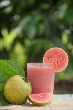 Guava suyu ya da bir bardakta Psidium Guajava ve yeşil yaprakların doğal bir arka planına sahip bir masada tüm ve dilimlenmiş guava ile süslenmiş.
