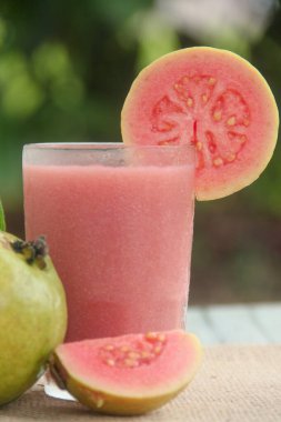 Guava suyu ya da bir bardakta Psidium Guajava ve yeşil yaprakların doğal bir arka planına sahip bir masada tüm ve dilimlenmiş guava ile süslenmiş.