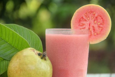 Guava suyu ya da bir bardakta Psidium Guajava ve yeşil yaprakların doğal bir arka planına sahip bir masada tüm ve dilimlenmiş guava ile süslenmiş.
