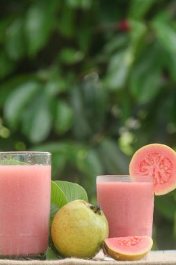 Guava suyu ya da bir bardakta Psidium Guajava ve yeşil yaprakların doğal bir arka planına sahip bir masada tüm ve dilimlenmiş guava ile süslenmiş.