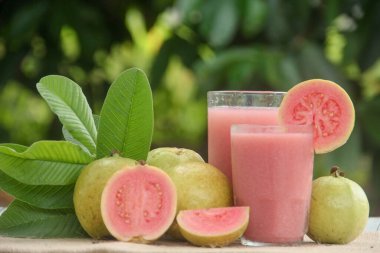 Guava suyu ya da bir bardakta Psidium Guajava ve yeşil yaprakların doğal bir arka planına sahip bir masada tüm ve dilimlenmiş guava ile süslenmiş.