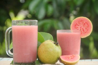 Guava suyu ya da bir bardakta Psidium Guajava ve yeşil yaprakların doğal bir arka planına sahip bir masada tüm ve dilimlenmiş guava ile süslenmiş.
