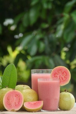 Guava suyu ya da bir bardakta Psidium Guajava ve yeşil yaprakların doğal bir arka planına sahip bir masada tüm ve dilimlenmiş guava ile süslenmiş.