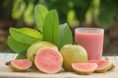 Guava suyu ya da bir bardakta Psidium Guajava ve yeşil yaprakların doğal bir arka planına sahip bir masada tüm ve dilimlenmiş guava ile süslenmiş.