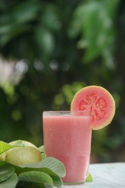 Guava suyu ya da bir bardakta Psidium Guajava ve yeşil yaprakların doğal bir arka planına sahip bir masada tüm ve dilimlenmiş guava ile süslenmiş.