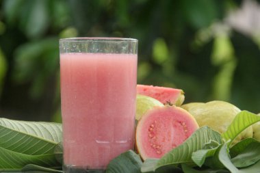 Guava suyu ya da bir bardakta Psidium Guajava ve yeşil yaprakların doğal bir arka planına sahip bir masada tüm ve dilimlenmiş guava ile süslenmiş.