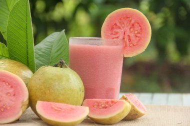 Guava suyu ya da bir bardakta Psidium Guajava ve yeşil yaprakların doğal bir arka planına sahip bir masada tüm ve dilimlenmiş guava ile süslenmiş.