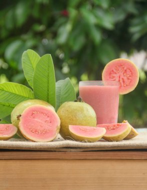 Guava suyu ya da bir bardakta Psidium Guajava ve yeşil yaprakların doğal bir arka planına sahip bir masada tüm ve dilimlenmiş guava ile süslenmiş.