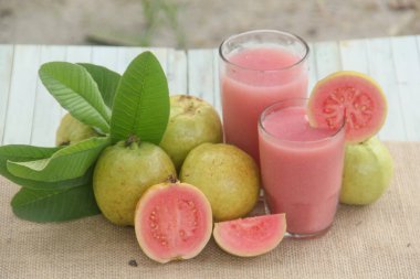 Guava suyu ya da bir bardakta Psidium Guajava ve yeşil yaprakların doğal bir arka planına sahip bir masada tüm ve dilimlenmiş guava ile süslenmiş.