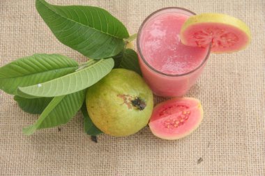 Guava suyu ya da bir bardakta Psidium Guajava ve yeşil yaprakların doğal bir arka planına sahip bir masada tüm ve dilimlenmiş guava ile süslenmiş.