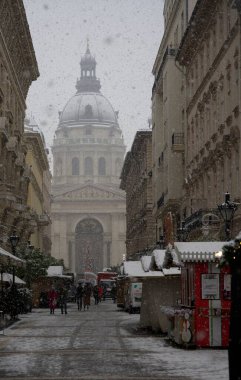 Budapeşte, Macaristan - 30 Kasım 2023: Yılbaşı pazarı ve alışveriş caddesinde karlı bir sabah, şenlik dekorasyonu ve arka planda Aziz Stephen Bazilikası