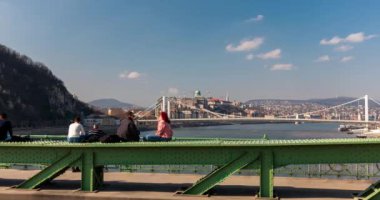 Budapeşte, Macaristan - 03 Mart 2024: Özgürlük köprüsünde oturan turistler. Arka planda Tuna nehri ve Buda kalesi var. Zaman aşımı