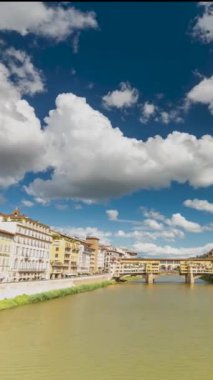 Florence, İtalya - 31 Mayıs 2024: Arno nehri üzerindeki Ponte Vecchio köprüsü. Zaman atlaması, kayma geçiş, dikey yönelim. Arka planda dinleme cihazı var. Orta bulutlu gökyüzü.
