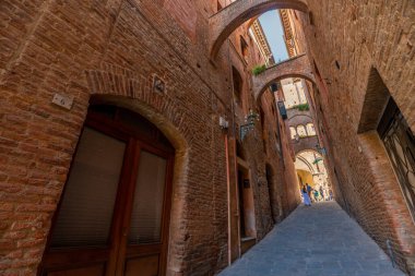 Siena, İtalya - 01 Haziran 2024: Siena 'nın güzel caddesi. Aşağıdan yukarıya doğru. Ön planda kemer olan ev..