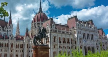 Budapeşte, Macaristan - 16 Haziran 2024: Sıcak bir günde parlamento binası. Hızlandırılmış, yakınlaştırılmış geçiş. Güneşli bir gün, orta bulutlu bir gökyüzü.