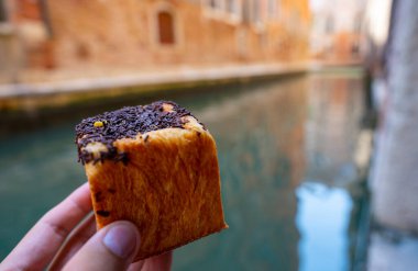 Venice, Italy - June 05, 2024: Chocolate Croissant in a cube shape. Venice canal on the background. clipart