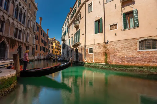 stock image Venice, Italy - June 05, 2024: A gondolier is waiting for tourists on the bridge over the canal. Popular tourist attractions in Venice. Long exposure shot.