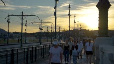 Budapeşte, Macaristan - 5 Temmuz 2024: Margit Köprüsü yaya şeridinde halk trafiği. Gün batımı. Yavaş çekim