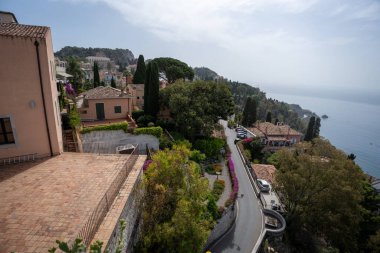 Taormina, İtalya - 19 Haziran 2024: Taormina 'nın kıyı cazibesine tepeden bakan. Terracotta çatıları ve yemyeşil şelaleler Akdeniz 'e doğru akıyor..
