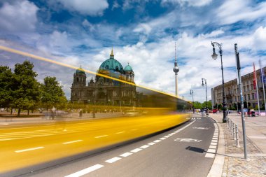 Berlin, Almanya - 22 Haziran 2024: Berlin katedrali ve B5 yolu. Arka planda TV kulesi var. Orta bulutlu gökyüzü. Uzun pozlu çekim. Sarı otobüsten hareket bulanıklığı.