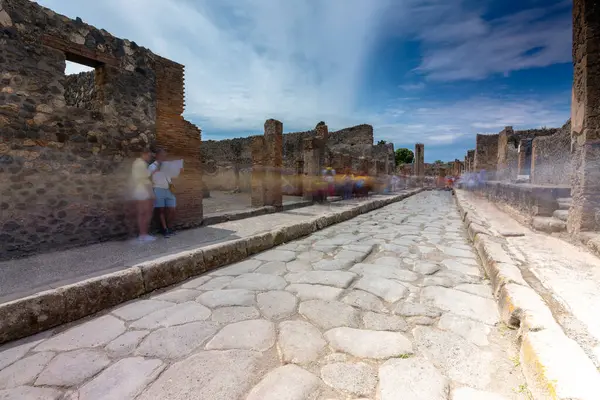 Pompei, İtalya - 25 Mayıs 2024: Pompei 'deki ana caddenin uzun pozlama sahnesi, geçen her turist ve hareketin yumuşak ışık izleriyle sessiz atmosferi yakalıyor.