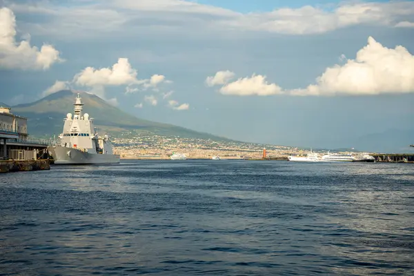 Napoli, İtalya - 26 Mayıs 2024: Napoli limanına yanaşan bir askeri gemi ve arka planda Vesuvius Dağı yer almaktadır..