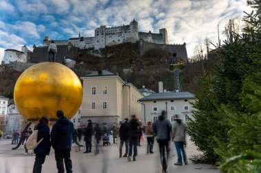 Salzburg, Avusturya - 21 Aralık 2024: Hohensalzburg arkaplanlı Stephan Balkenhol 'un Sphaera altın küre sanat kurulumu. Uzun pozlama