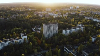 İHA, terk edilmiş Pripyat şehrinden geçiyor. Yıkılmış binalar. Şehrin aşırı gelişmiş caddeleri. Sonbahar renkleriyle Çernobil Hava Aracı Videosu - Günbatımı